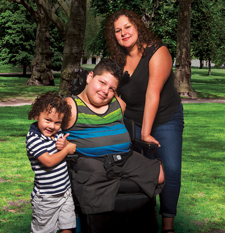 a boy in a wheelchair flanked by his mother and younger brother