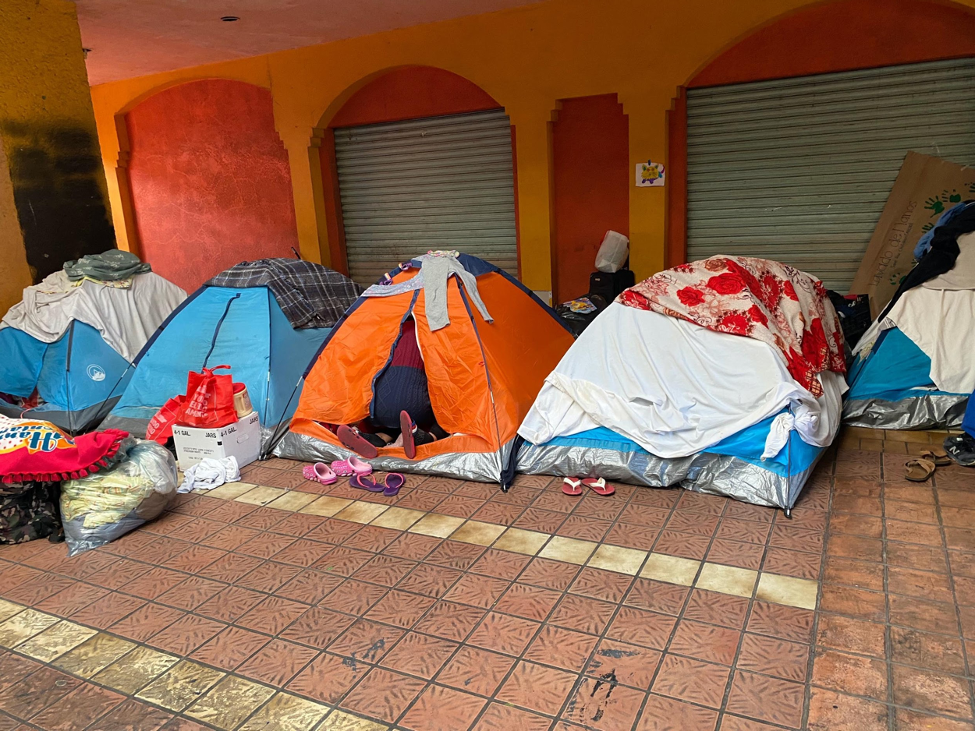 Five tents lined up next to each other on the ground in front of a closed building.