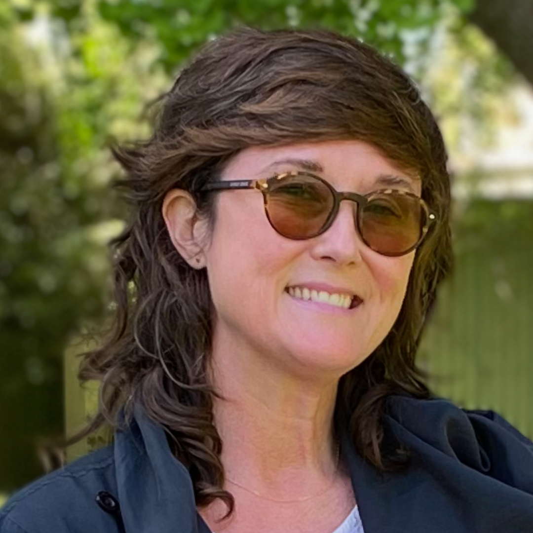 Close up headshot of an individual wearing glasses and a collared shirt looking afar in front of a tree outside