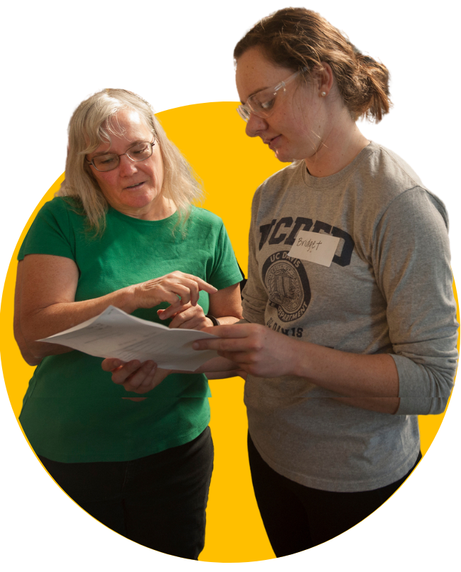 Two women are looking down at a notebook together designed as a circular graphic with a gold background