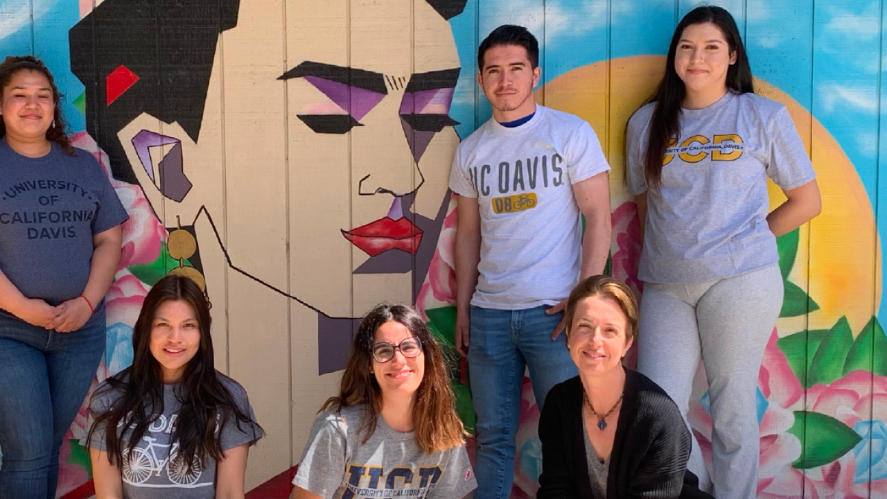 A group of people pose in front of a mural of Frida Kahlo