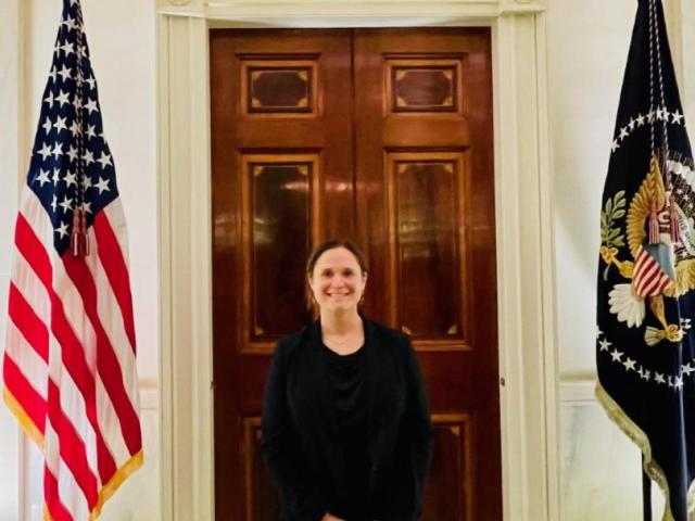 Woman standing in front of a door at the White House in between two flags