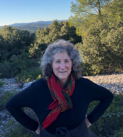 Diane Ullman smiling in front of a nature scenery. She wears a red scarf and a black long-sleeves shirt.
