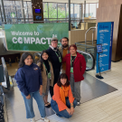 Group of six individuals smile for a photo inside the lobby of a building at the Campus Compact conference.