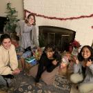 Four young women sit in front of bags of groceries in a decorated holiday living room