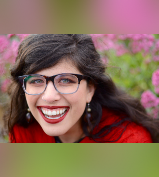 woman wearing glasses smiling for a close up in front of flowers