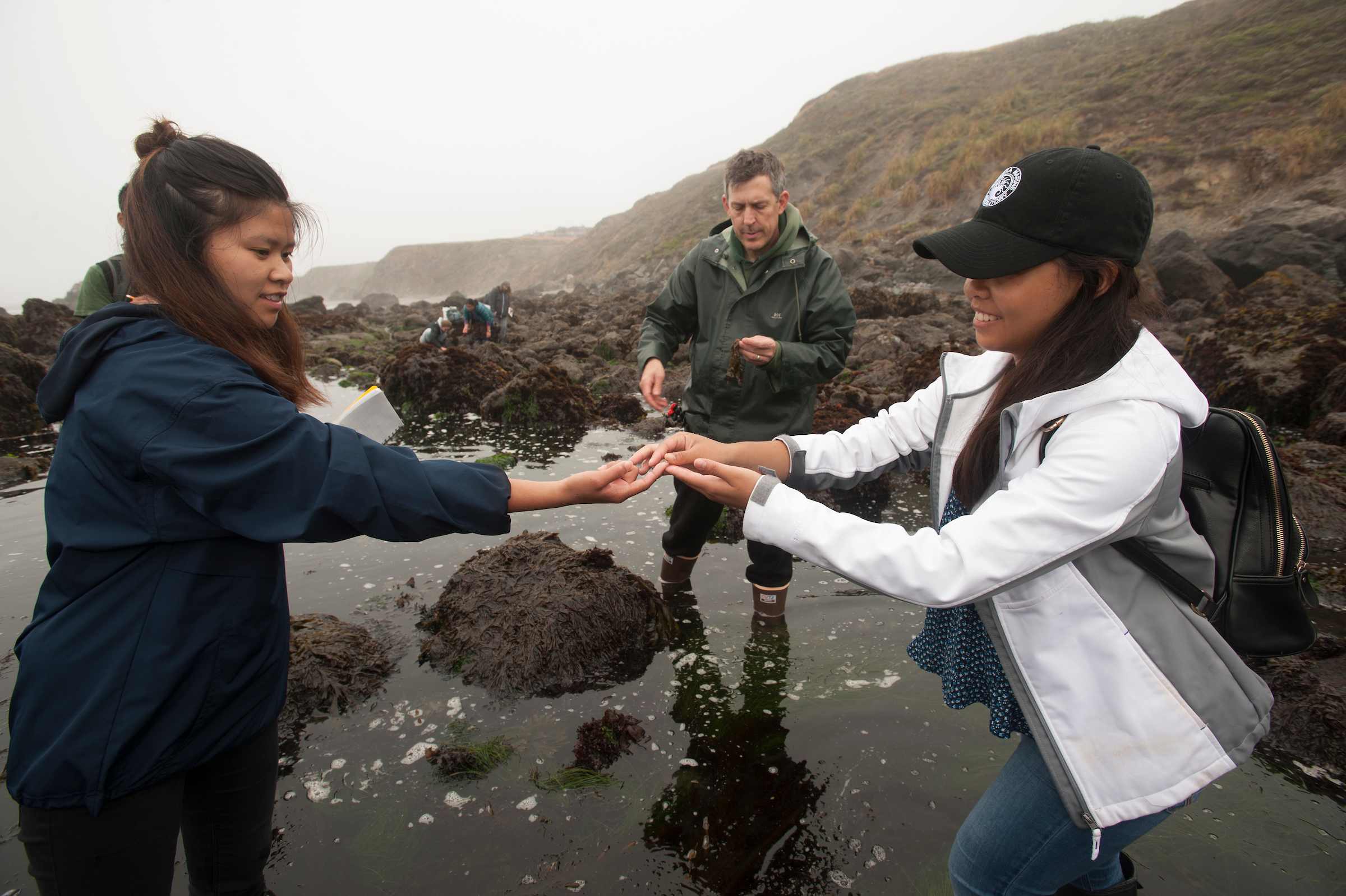 Two students exchange finds by holding out their hands. They stand in the water. Photo taken by Gregory Urquiaga. 