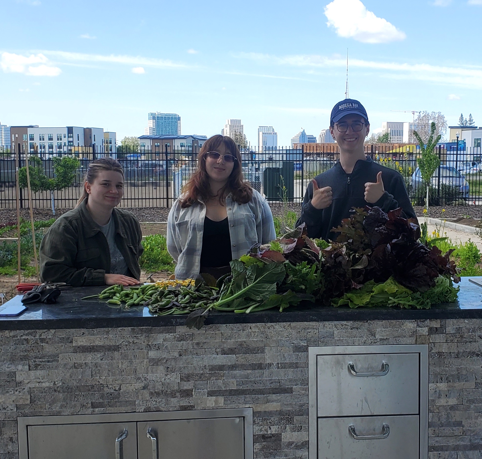 Three students stand and smile behind vegetables that they proudly display