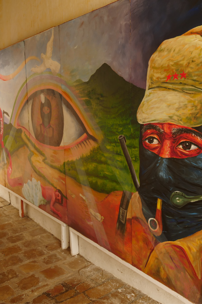 Colorful mural that encompasses an eye with a person inside the eye. To the right of the eye is a man wearing a hat and a headset with a microphone. 