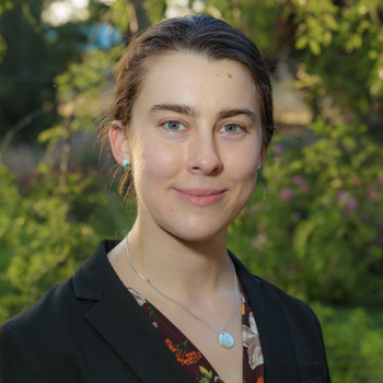 woman wearing a blazer smiling directly into the camera outside