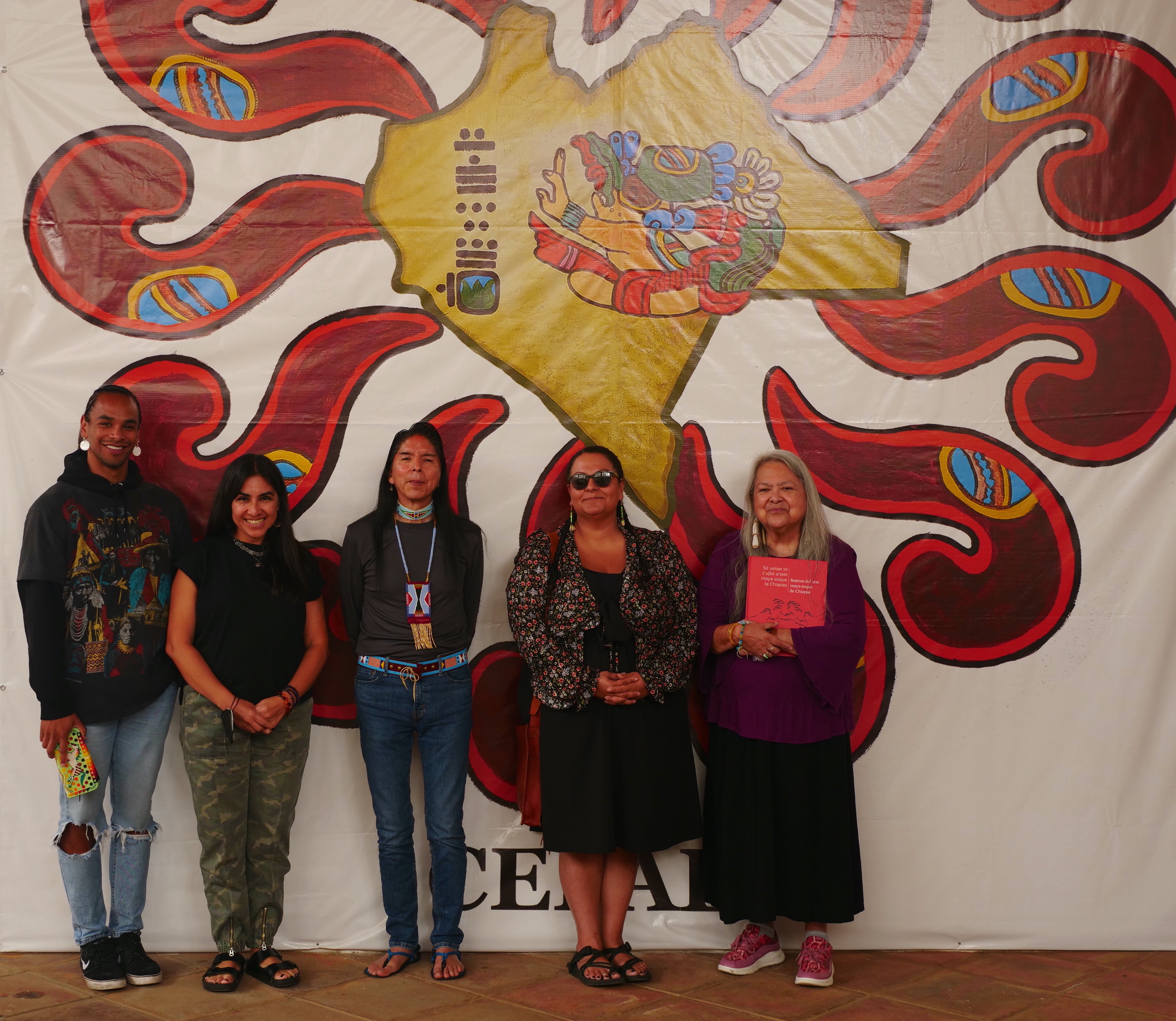 Five individuals standing side by side and smiling in front of a colorful mural