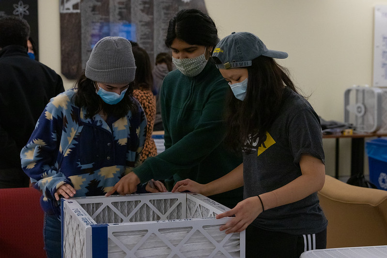 three students gather together around a box