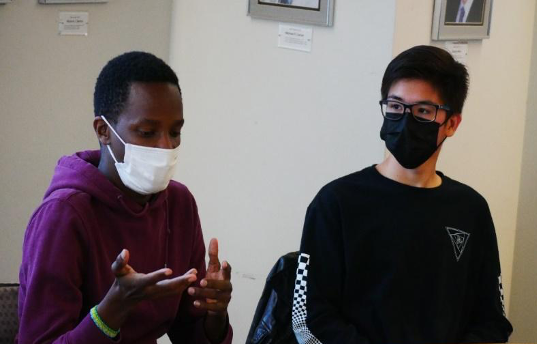 Two men wearing masks engaging in conversation inside a building