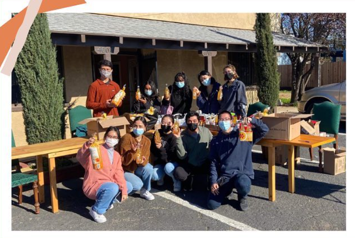 A group of students wearing mask hold various types of food during their food drive. 