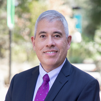 Man wearing a suit and purple polka dotted tie smiles outside for a close up photo