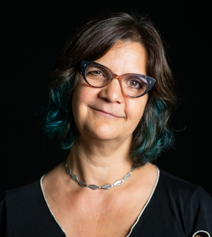 Headshot of Julie Wyman. A woman in front of a dark background. She is wearing glasses, a necklace, and a dark blouse.