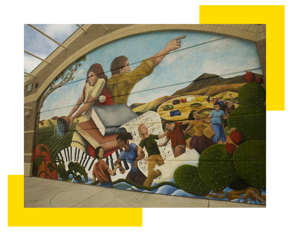 Graphic of a large mural on the back wall of Woodland High School's theater building featuring a woman with her back against a man. The man is facing away and points to the right. The woman holds a bowl and pours water to a field. They are behind large books, music notes and piano keys. Surrounding them are children holding arms and dancings. The mural is colorful and vibrant.