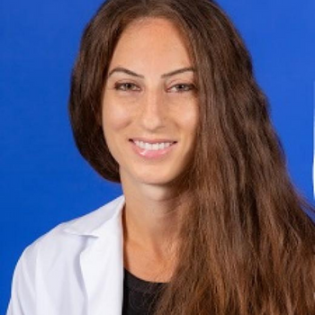 woman in a white lab coat smiling in front of a blue background
