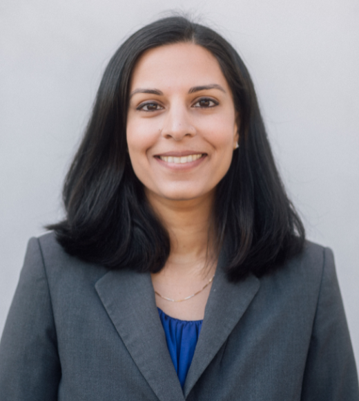 Close up headshot of a woman wearing a blazer in front of a plain background