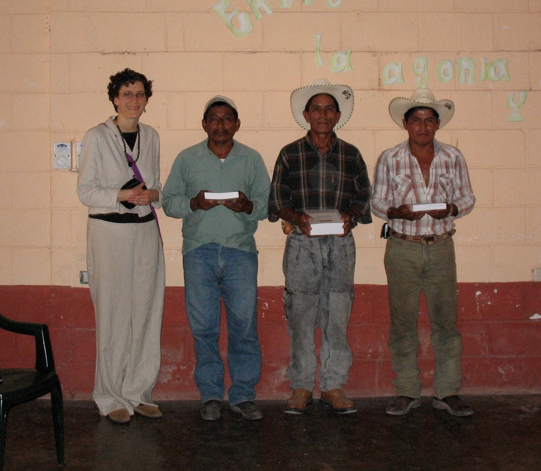 Liza Grandia stands for a group photo with three men in collared shirts and jeans. The three men stand in front of a wall and are holding a book.