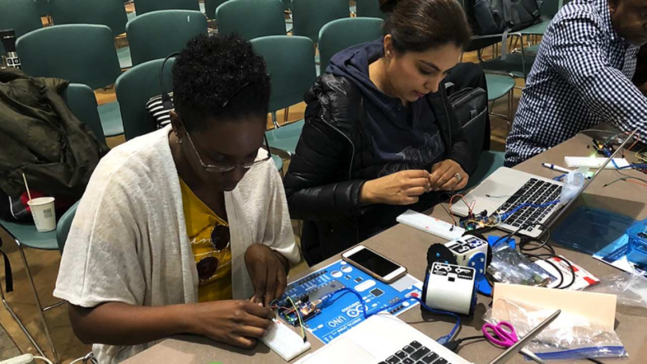 Two girls are working on a table next to each other and they are working with circuit boards and have laptops open in front of them as well 