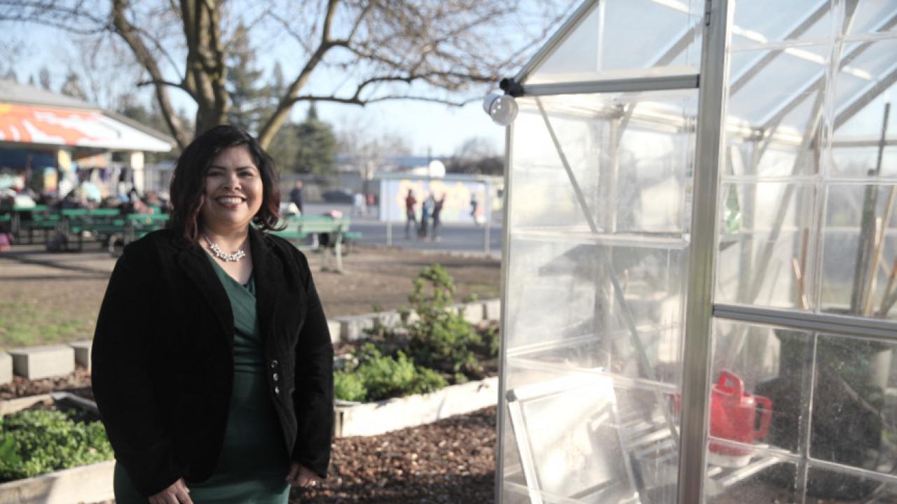 woman smiling while standing in front of a greenhouse at a school