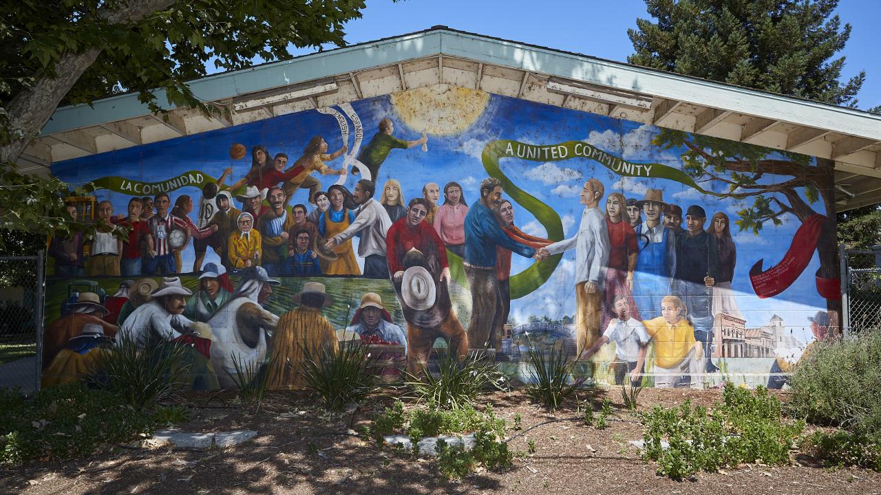 colorful mural on a side of a building that features different people together as a group with the words "la comunidad" and "a united community"
