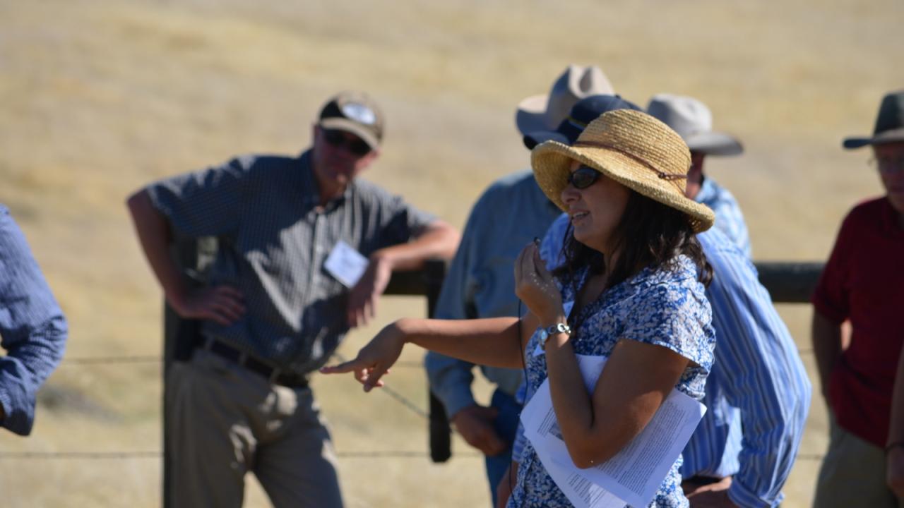 a woman in a straw hat pointing with papers in her arm 