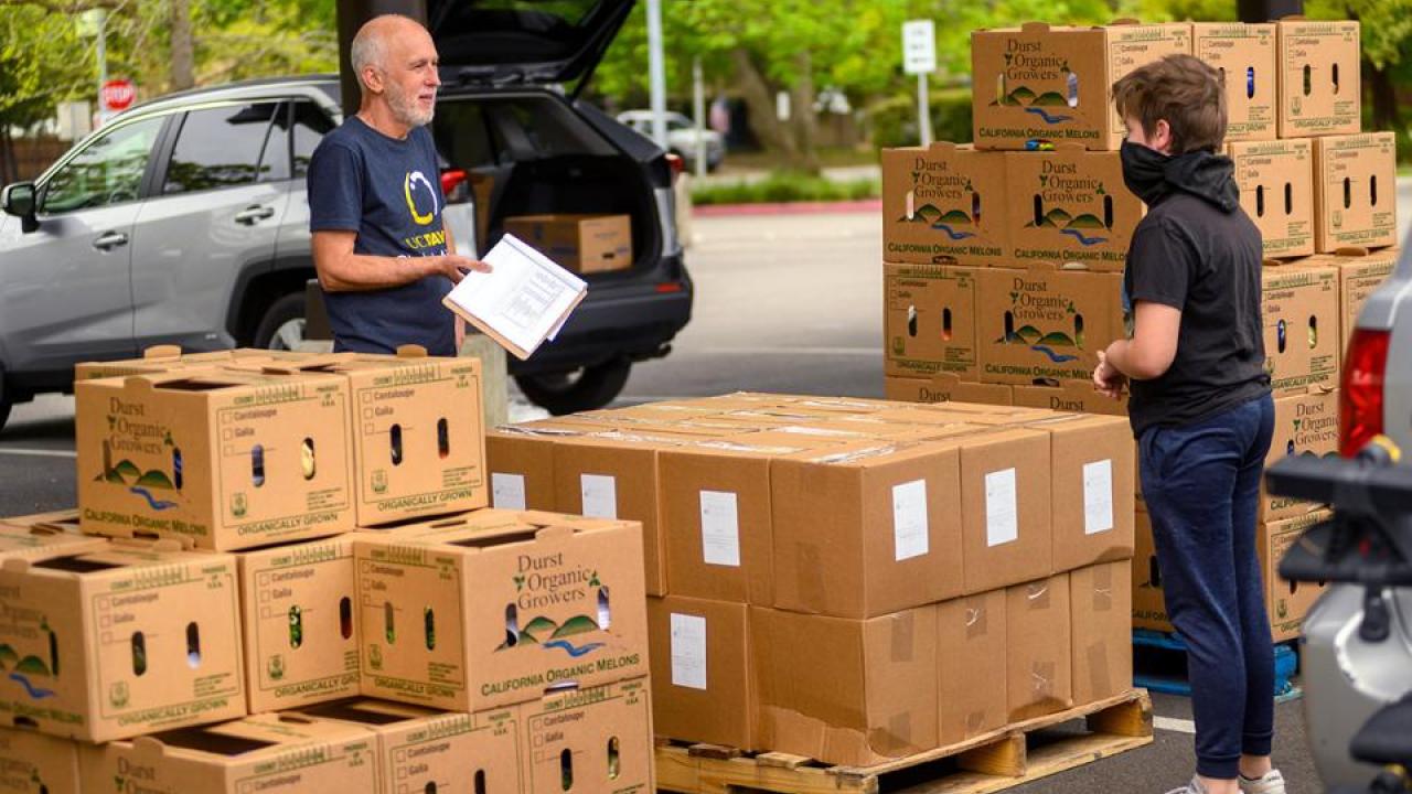 Robb Davis standing behind boxes with a clipboard talking to a woman