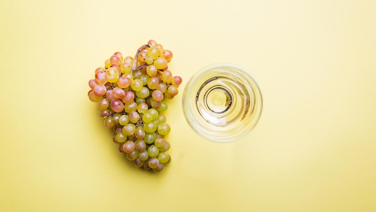 chardonnay grapes and a glass of wine on a yellow background