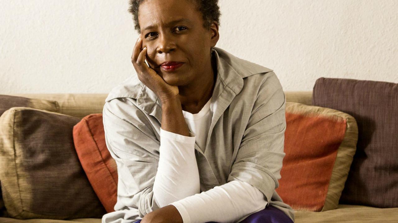 an african american woman seated on a couch holding her head in her hand