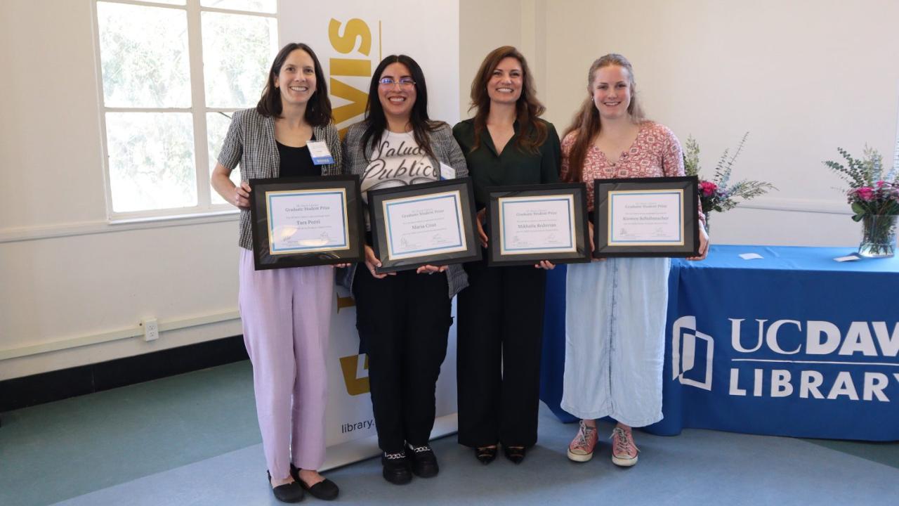 Four graduate students stand side by side, smiling and holding their awards