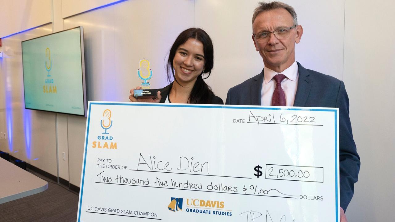 Student, Alice Dien, stand with J.P. Deplanque. Alice holds a grad slam award. They both hold a large check for the amount of $2,500.