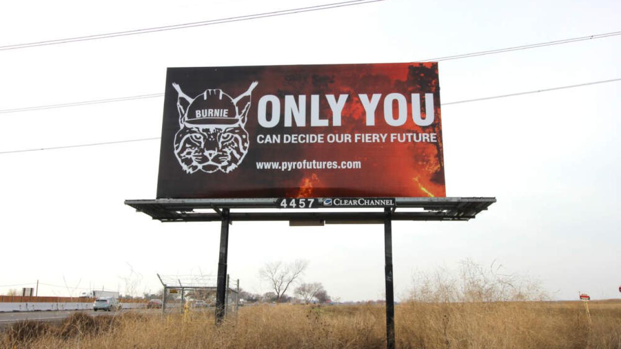 A billboard with Burnie the Bobcat on it that says "ONLY YOU CAN DECIDE OUR FIERY FUTURE" with link to "www.pyrofutures.com"