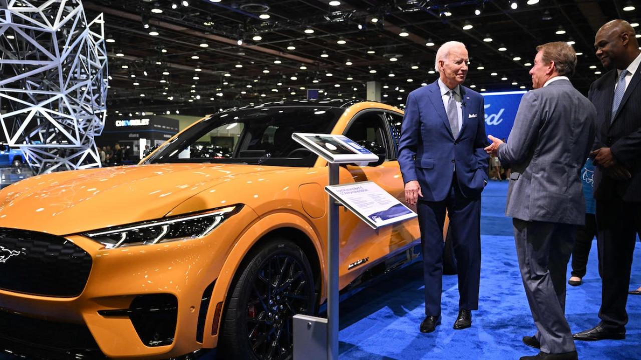 A bright yellow electric Ford Mustang car next to Joe Biden and two other men.