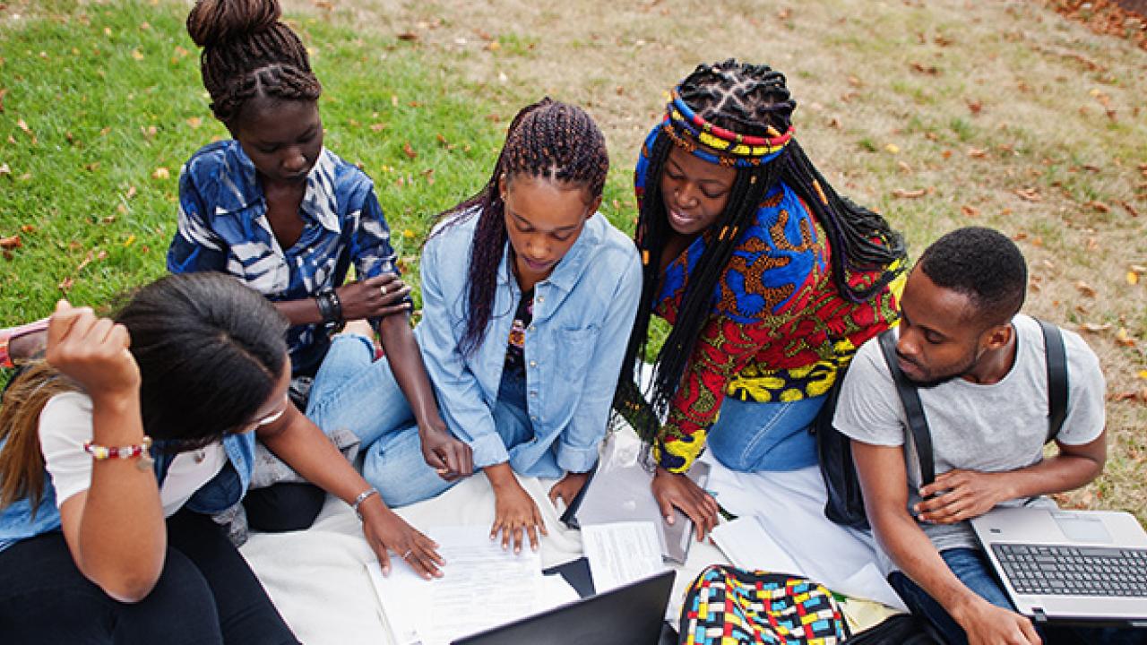 Group of five Black college students studying on the lawn
