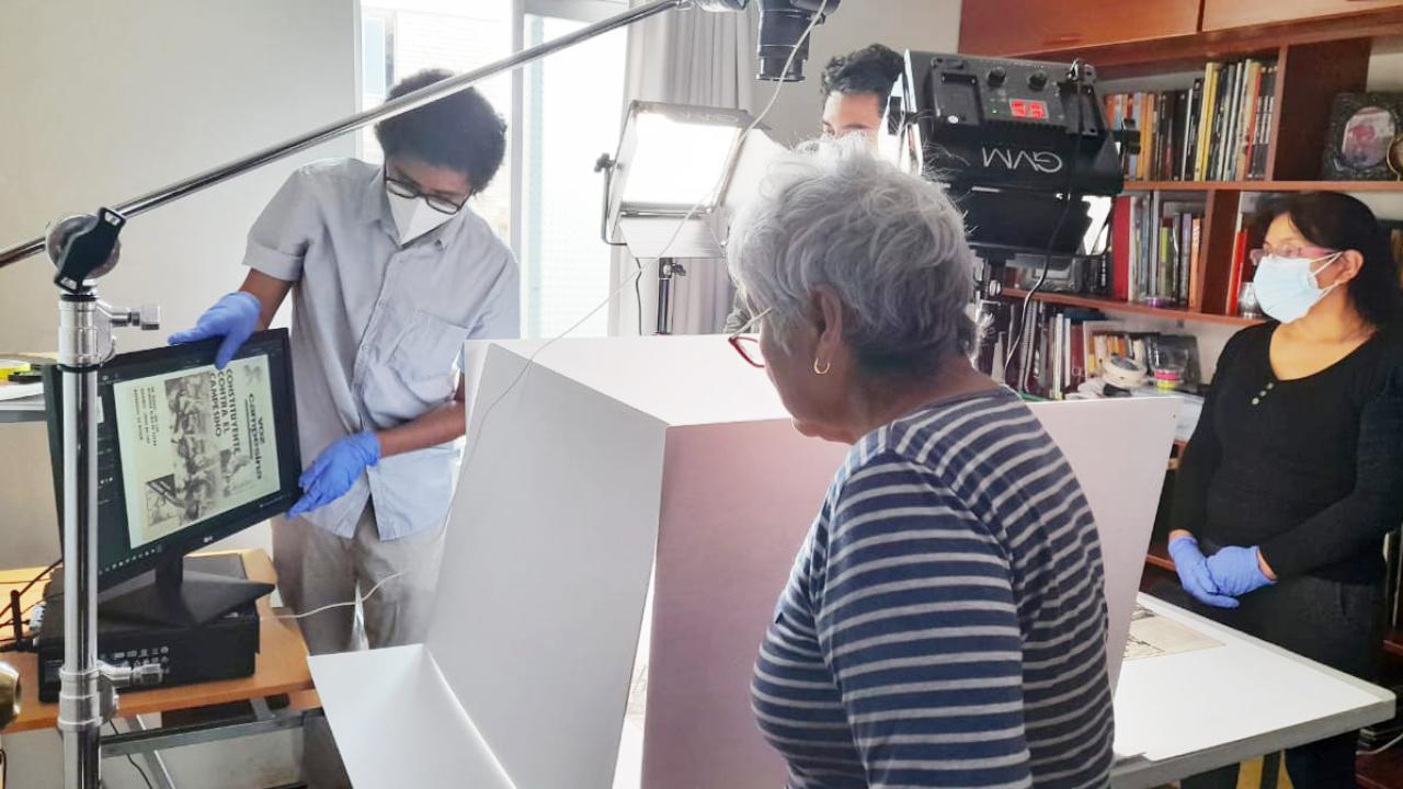 Research team stand around historical documents as they digitize it in a room filled with books