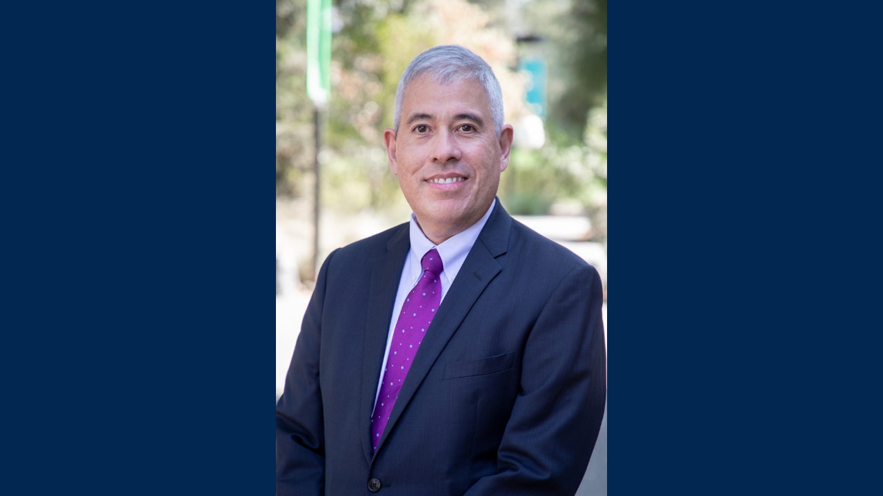 Man wearing a suit and purple polka dotted tie smiles outside for a close up photo