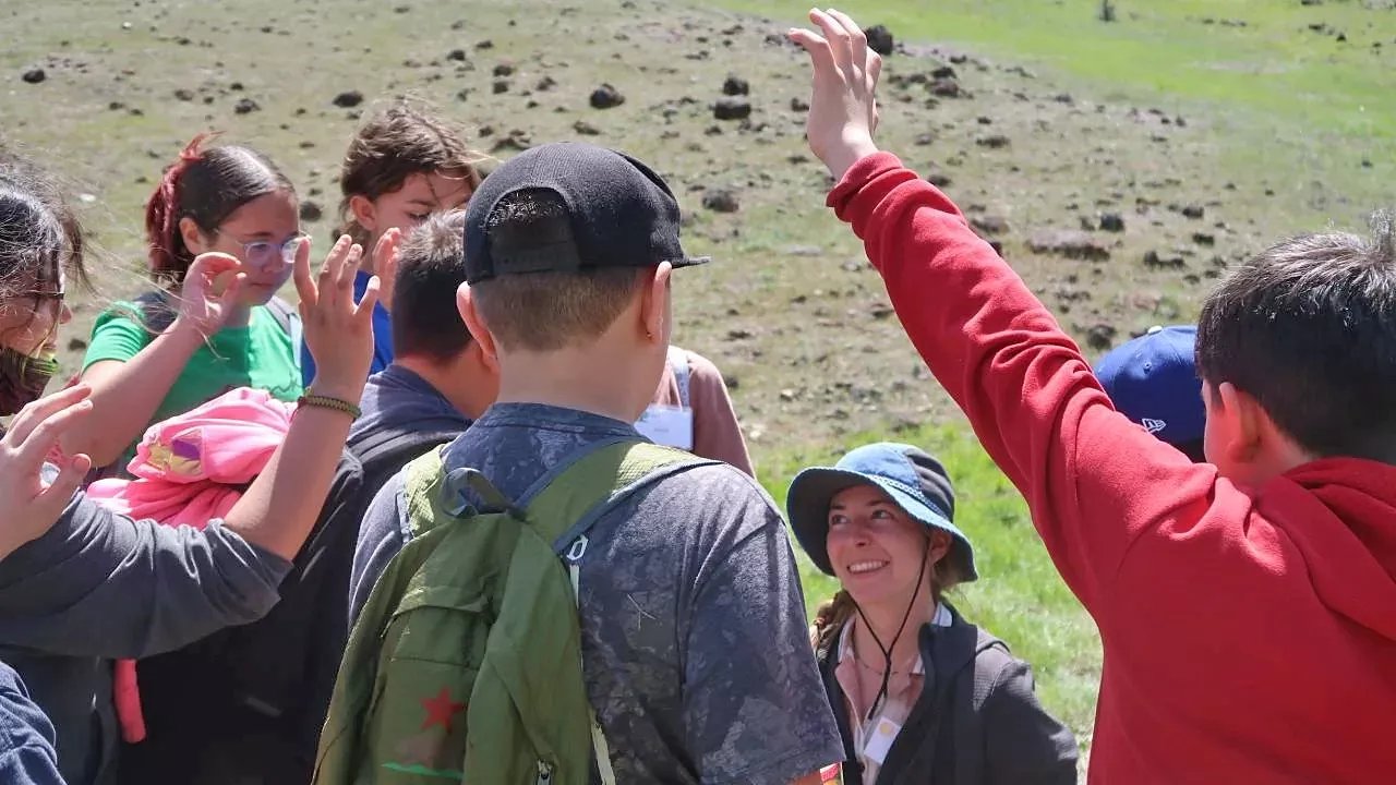 KiDS, a volunteer program, empowers the next generation of scientists. Group of students raise their hands outside.