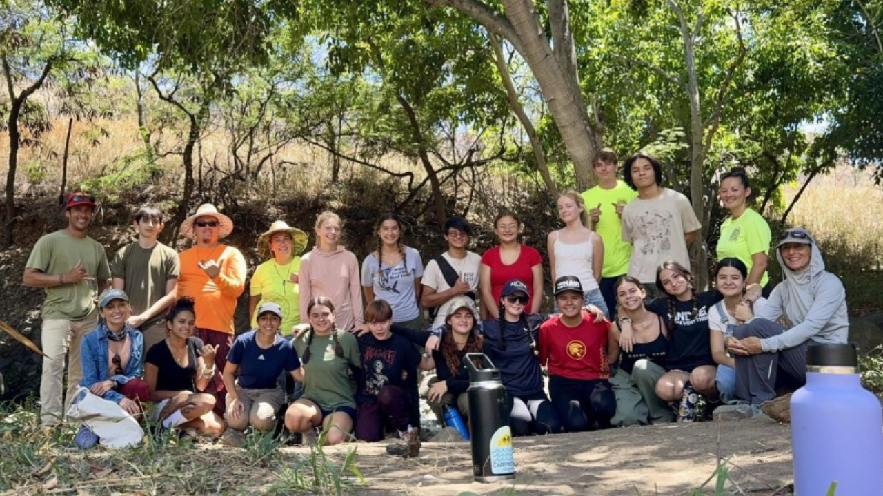 A group of students and adults pose together under a tree.