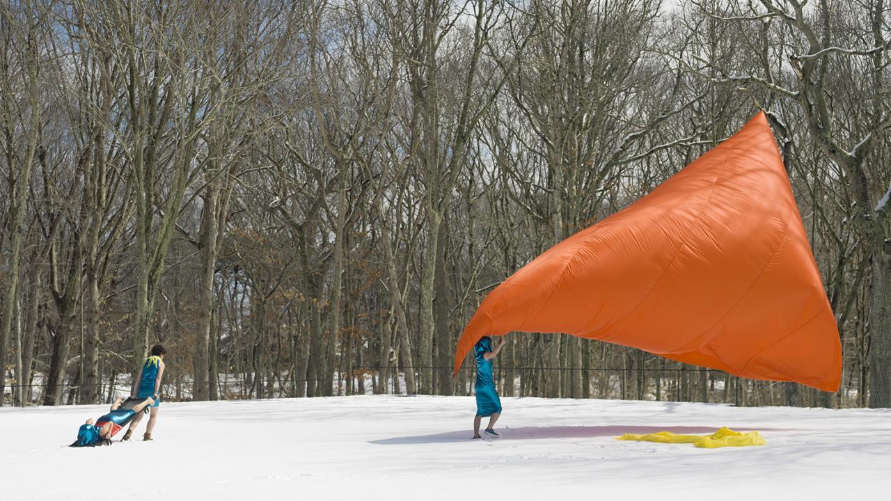 a snowy field with people spread out holding a large orange cloth