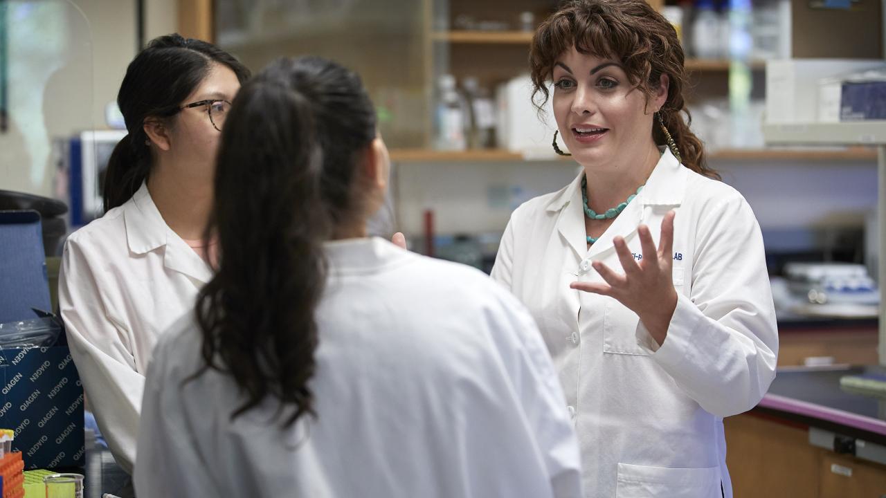 Woman in white lab coat talks to two other women in white lab coats