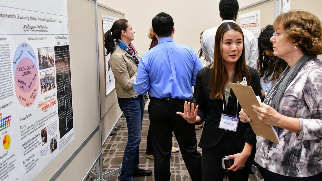 Poster presentation at the Scholarship of Teaching and Learning Conference. Student in professional attire talks about her poster to another woman who is holding a clipboard.
