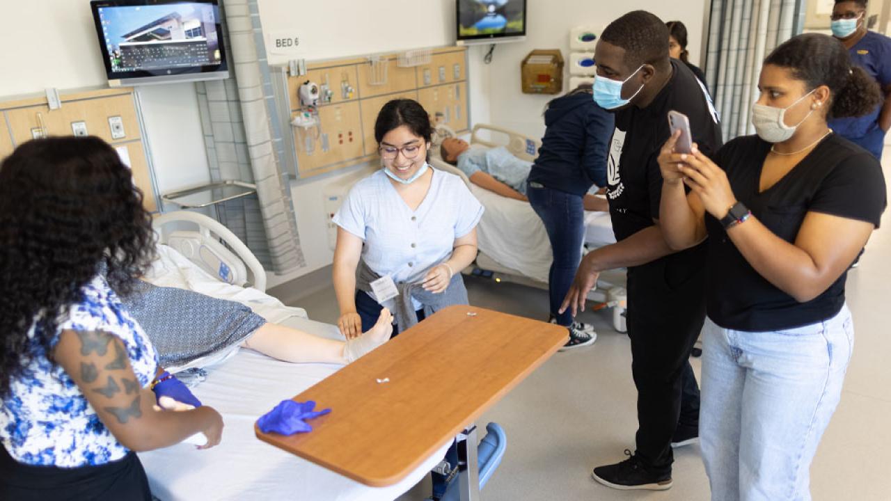 High school students use stethoscopes to hear body sounds from manikin in hospital simulation room
