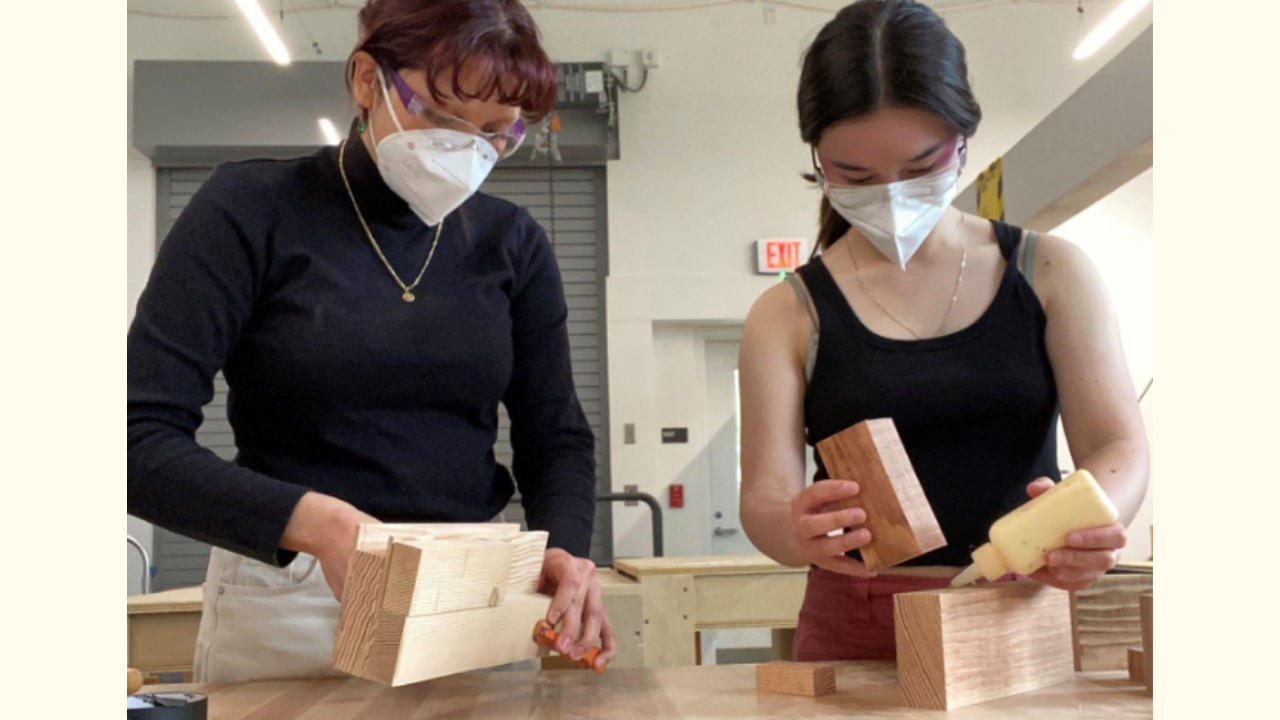 Students holding blocks to build a block scale model while wearing masks and safety glasses