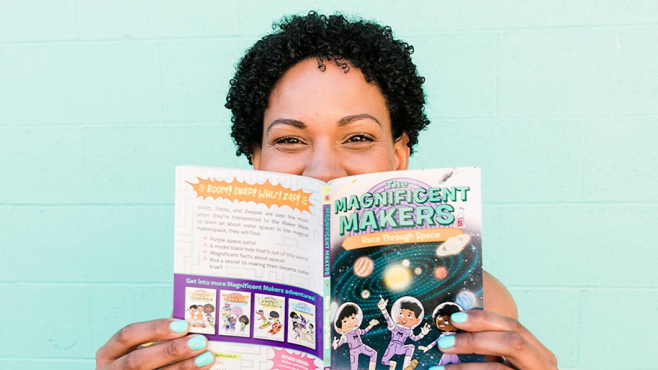Close up photo of Theanne Griffith smiling while holding a book titled "The Magnificent Makers"
