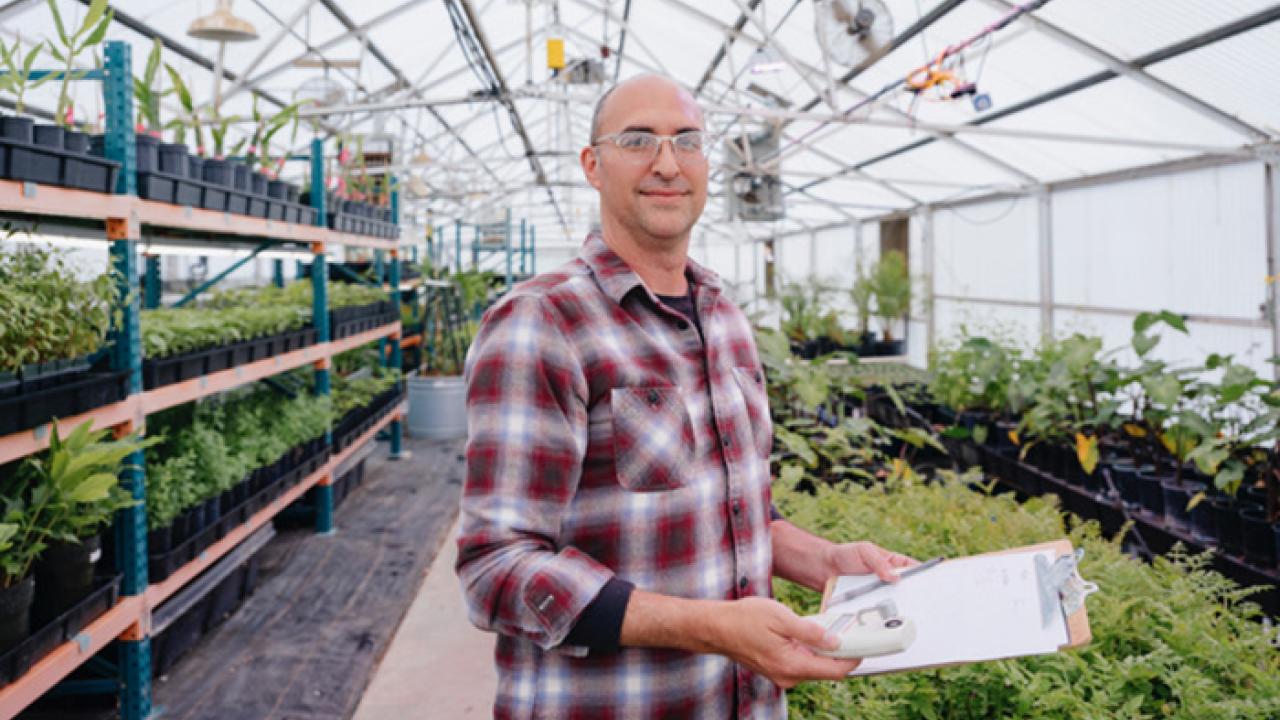 Man holding clipboard inside of a greenhouse smiles