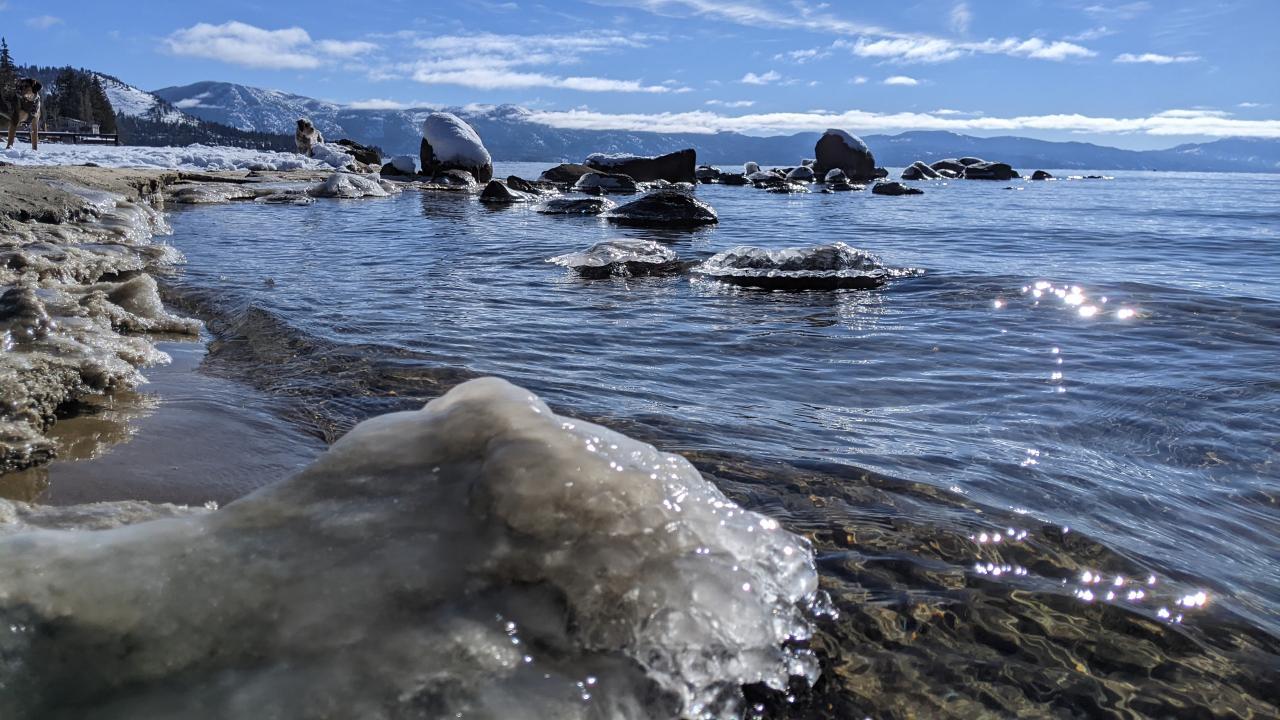 Lake Tahoe in winter with snowy mountains and clear sky with clouds in the background