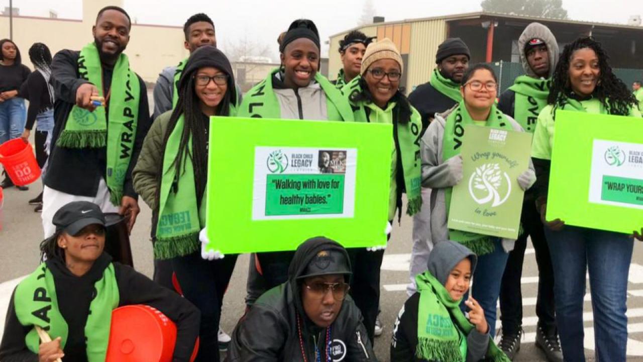 a group of young african-american men and women wearing bright green scarves and holding posters that read "walking with love for healthy babies"