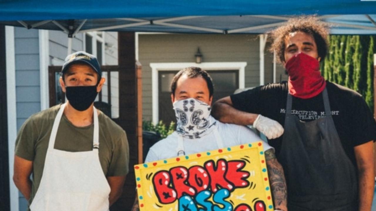 three men with masks and cooking aprons pose for a photo